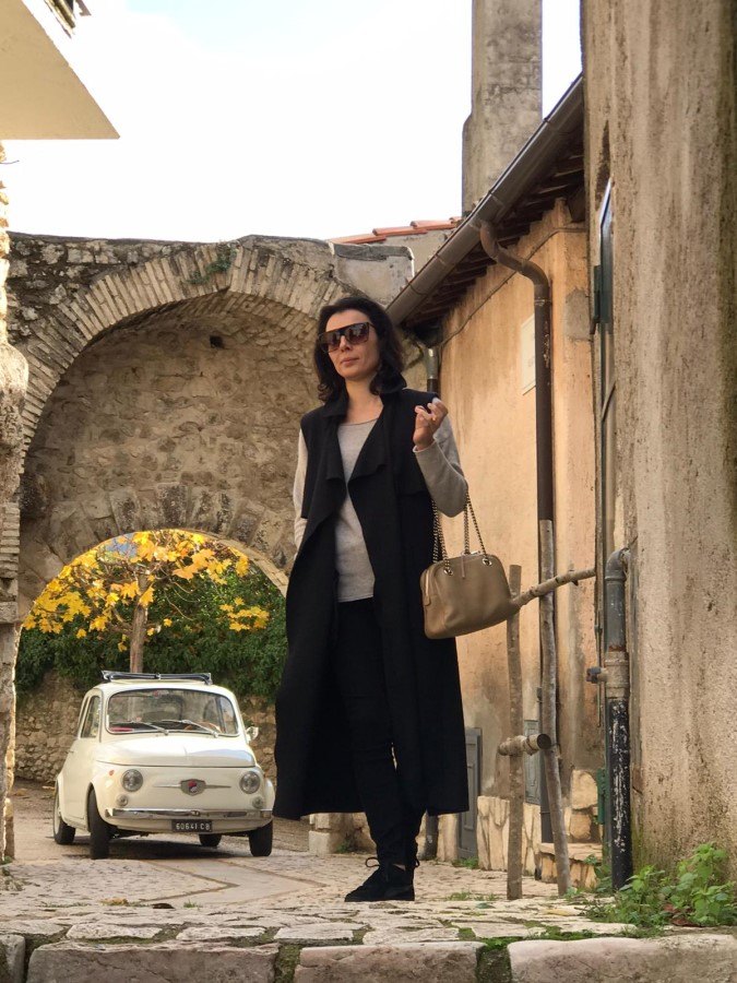 Woman standing in an alleyway with a white vintage Fiat 500 under a stone archway